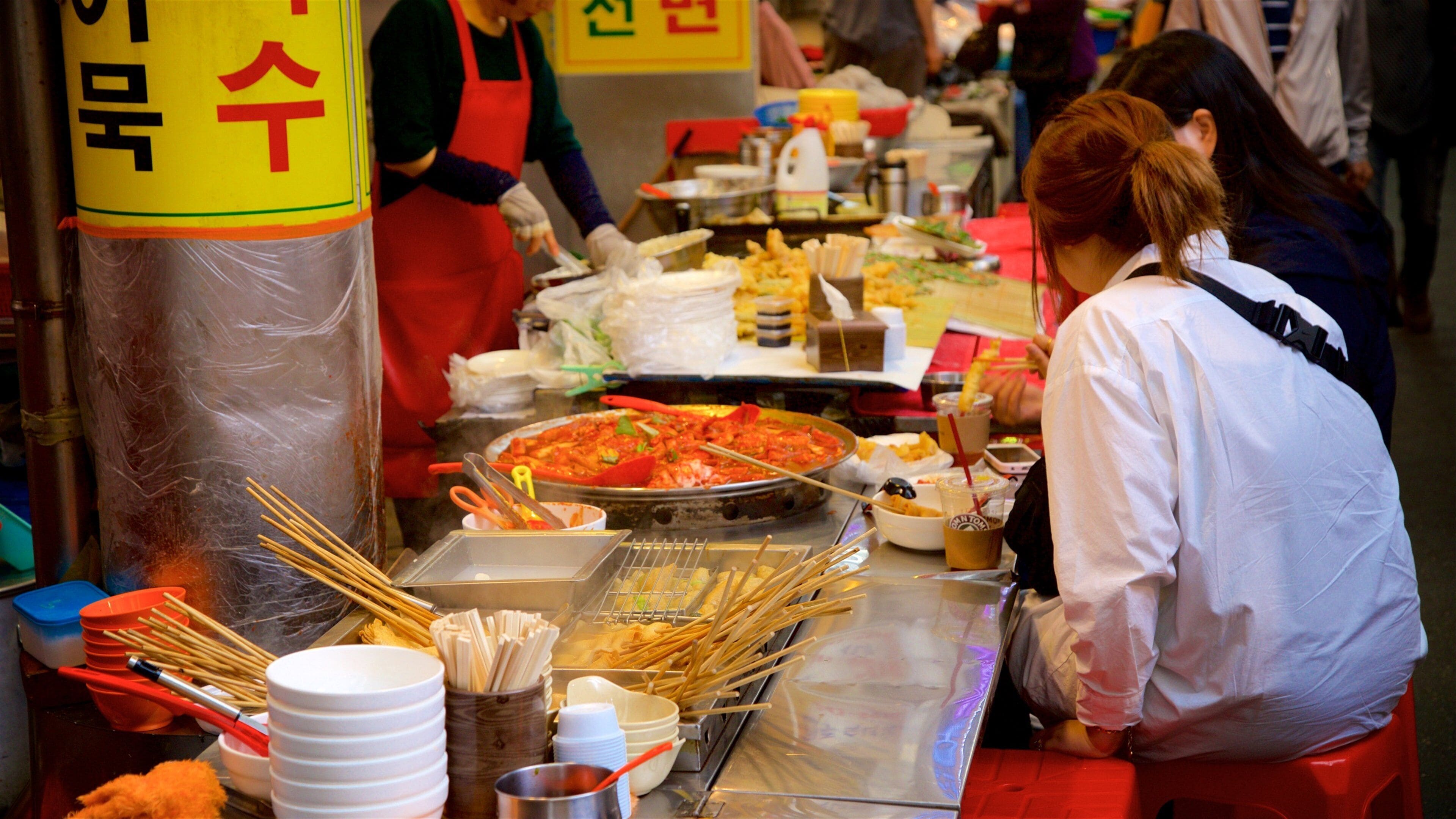 A food stall with a variety of dishes, utensils, and a large pan of food.