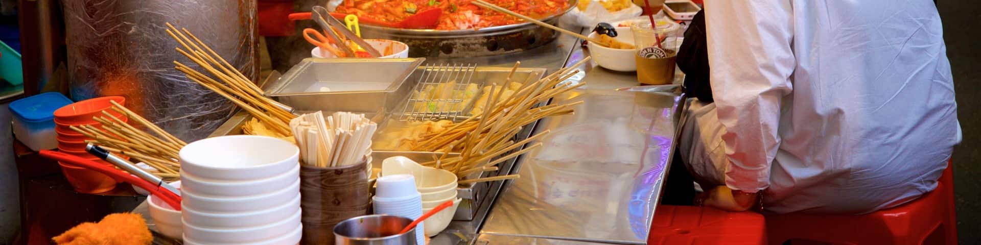 A food stall with a variety of dishes, utensils, and a large pan of food.