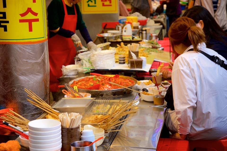 A food stall with a variety of dishes, utensils, and a large pan of food.