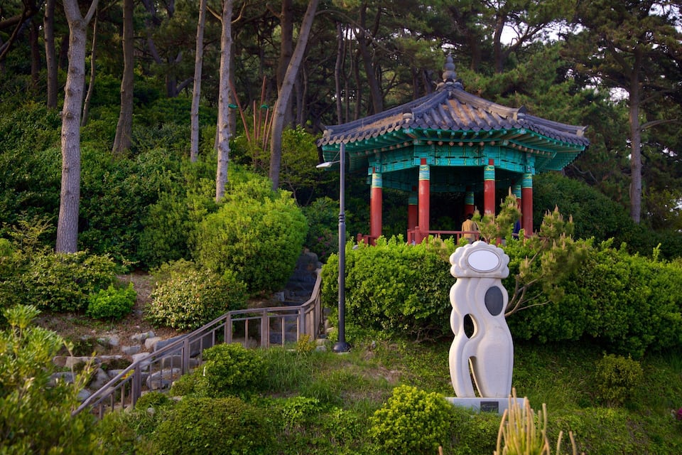 A traditional pavilion with a tiled roof, surrounded by lush greenery and trees.