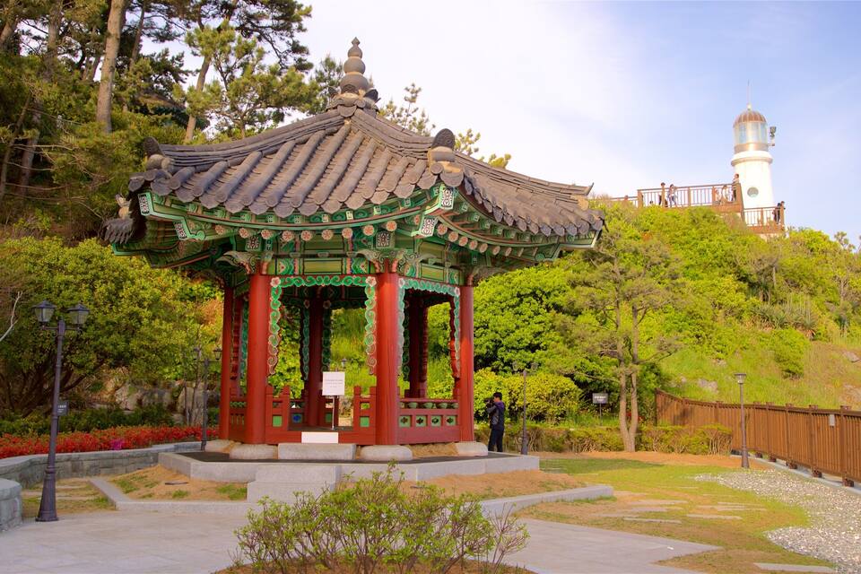 A traditional pavilion with a tiled roof, surrounded by lush greenery and a stone pathway.