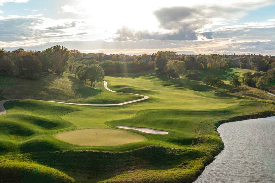 A golf course with a water body and houses in the background.