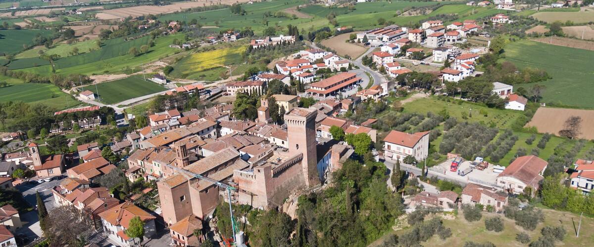 An aerial view of a historic town with red-roofed buildings, a prominent tower, and surrounding green fields.
