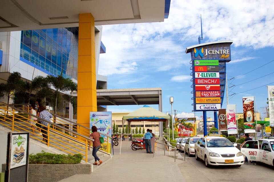 Una calle concurrida con un anuncio del centro comercial J Centre, un hipermercado y varios otros negocios.