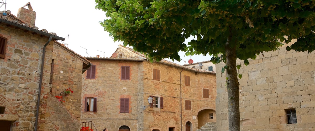 A stone building with red shutters, a tree in the foreground, and a staircase leading to an upper level.