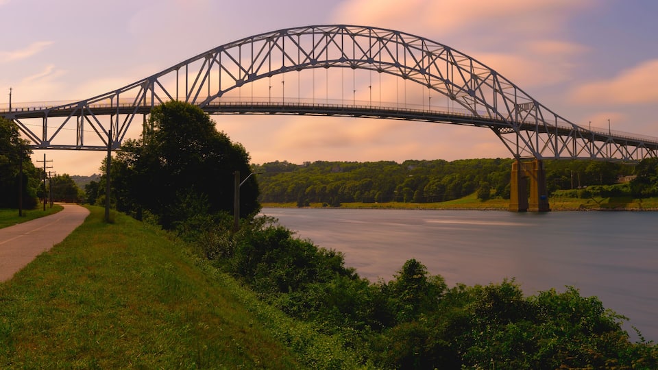 A steel truss bridge over a river with a path beside it.