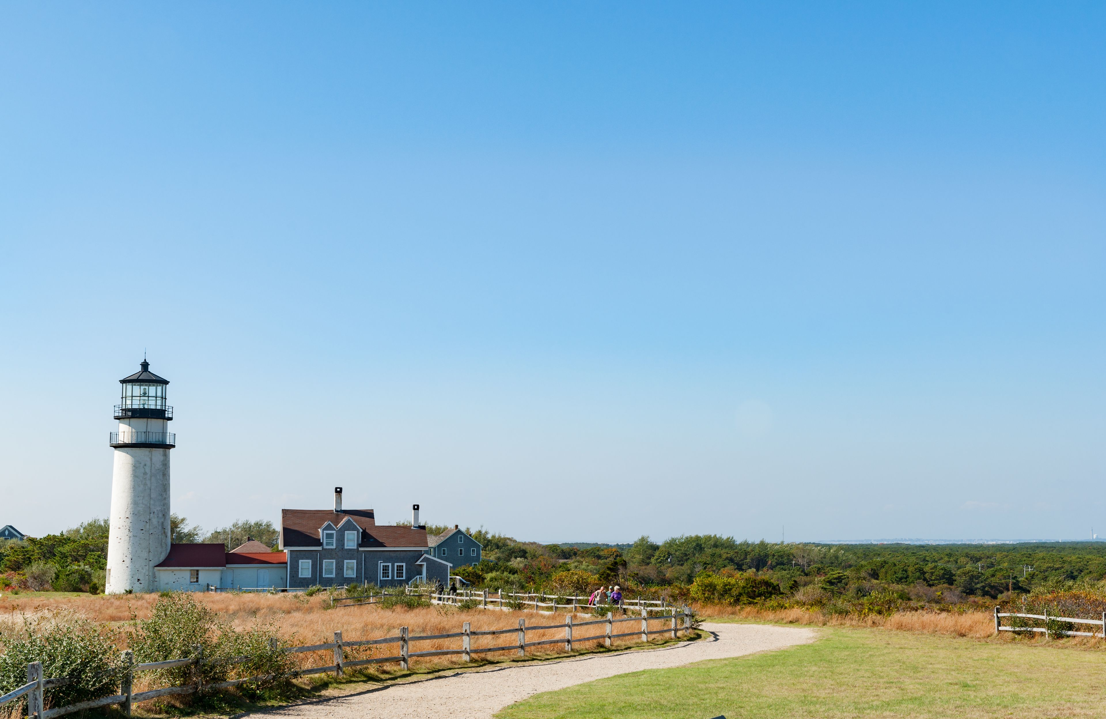 A lighthouse, a house, and a wooden fence in a coastal landscape.