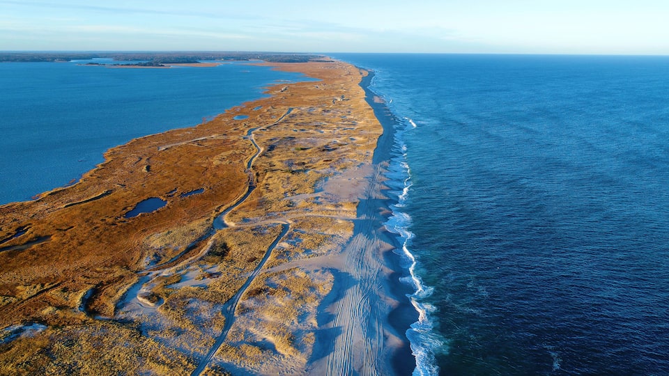 A coastal landscape with a sandy beach, a winding road, and a large body of water.