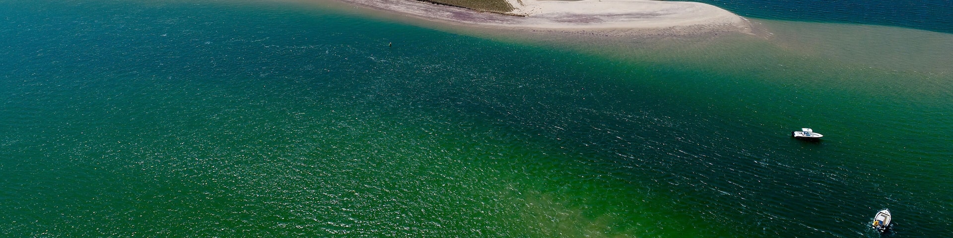 A coastal landscape with a prominent sandy peninsula surrounded by turquoise waters.