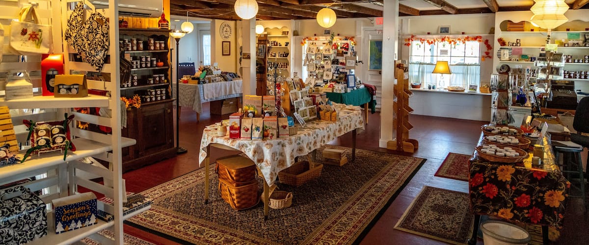 A cozy, rustic shop interior with wooden beams, patterned rugs, and various items on display including bags, jars, and greeting cards.