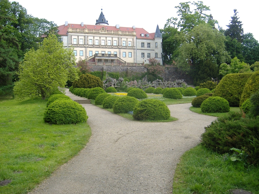 Ein formeller Garten mit Kiesweg, ordentlich geschnittenen Büschen und einem großen historischen Gebäude im Hintergrund.