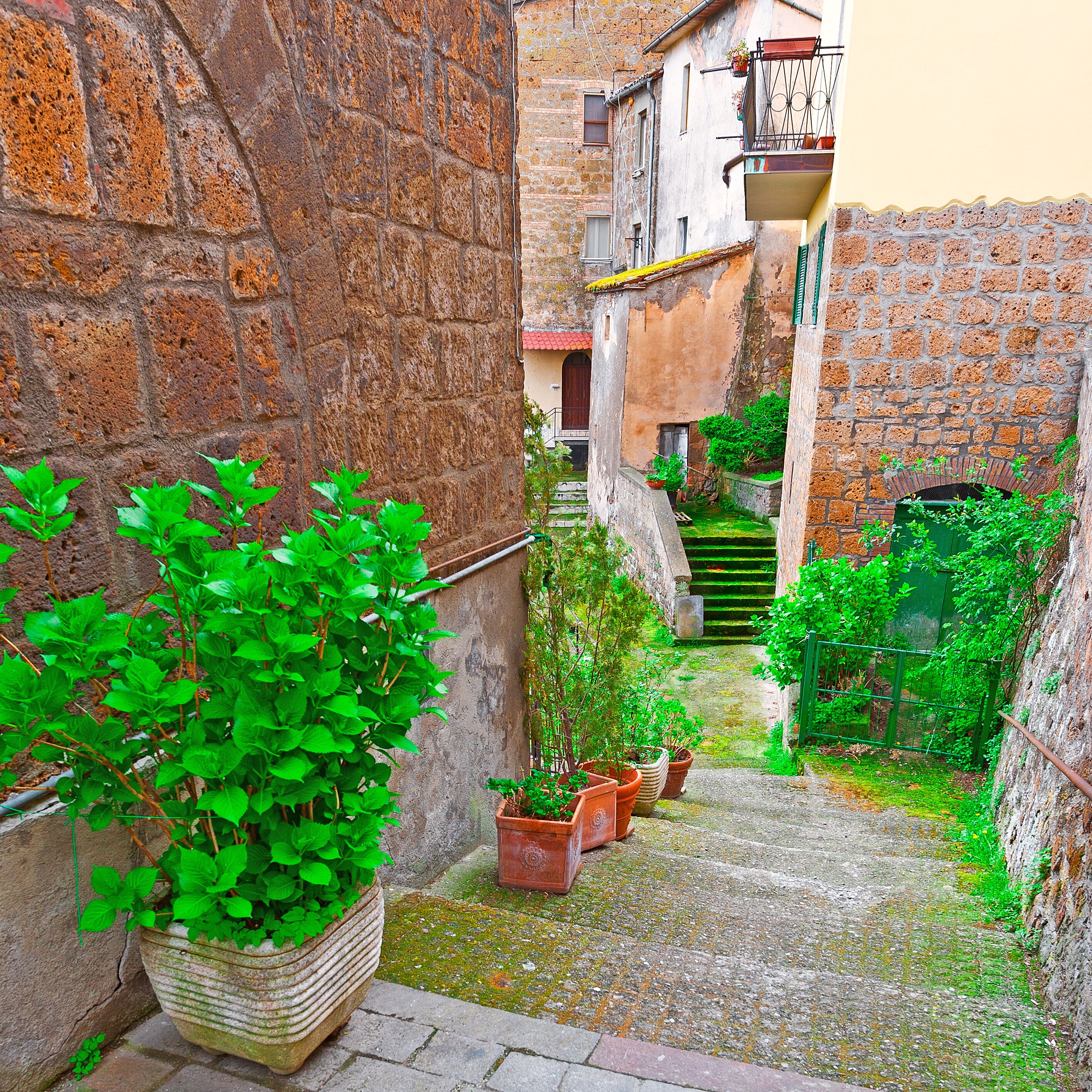 A narrow alley with stone walls, potted plants, and a staircase leading to a building.