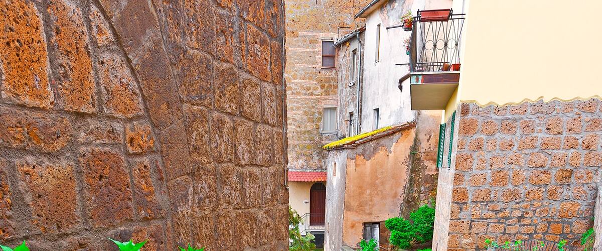 A narrow alley with stone walls, potted plants, and a staircase leading to a building.
