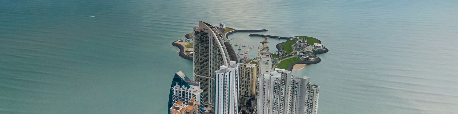 Paisagem costeira com edifícios altos, um porto de iates e uma praia.