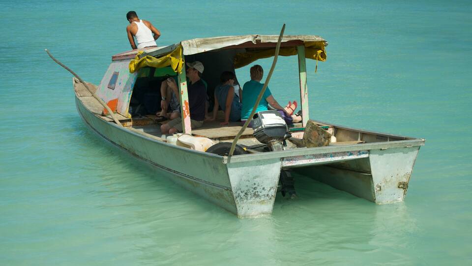 A small, weathered boat with people on it, floating on clear turquoise water.