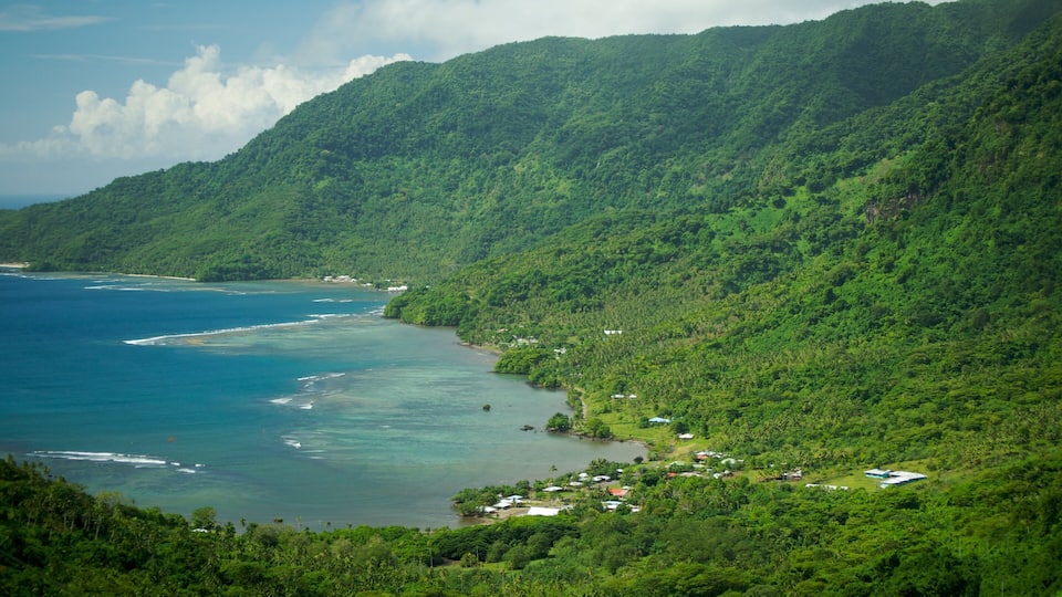 A coastal landscape with lush green hills, a clear blue sea, and small buildings near the shore.