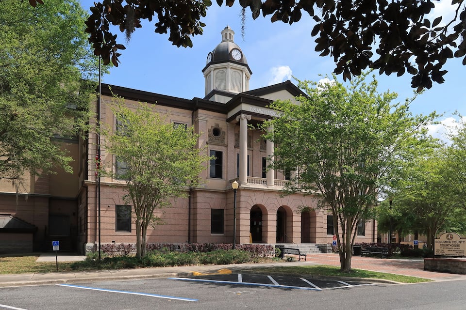 A courthouse with a clock tower, surrounded by trees and a parking lot.