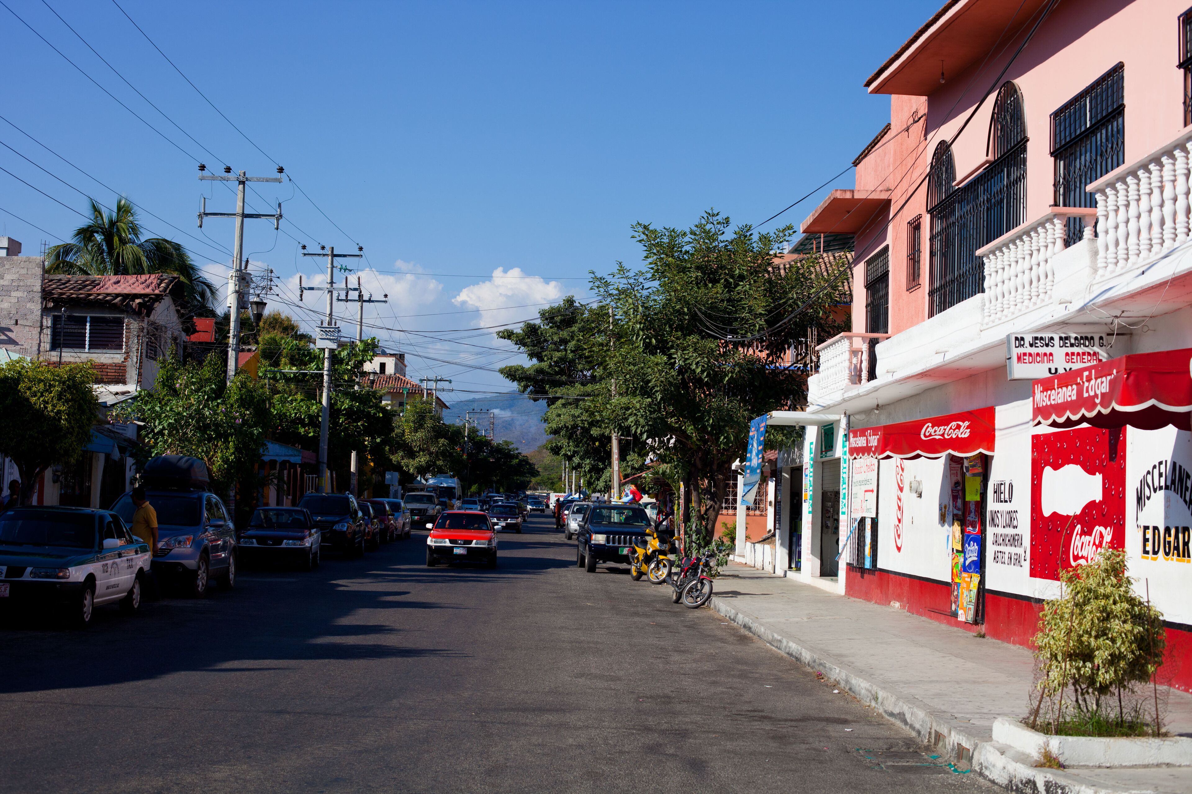 A street with parked cars, a bicycle, and a building with a Coca-Cola sign.