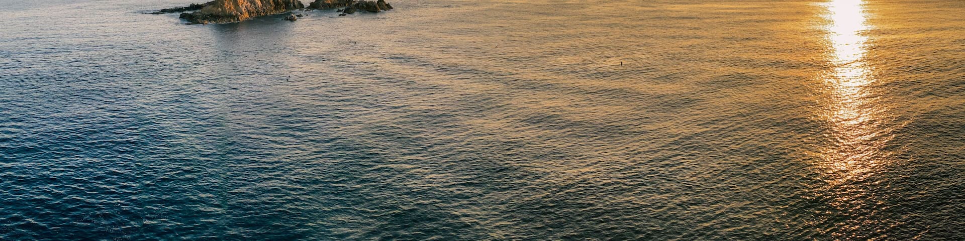 A coastal landscape with a rocky outcrop and calm sea at sunset.