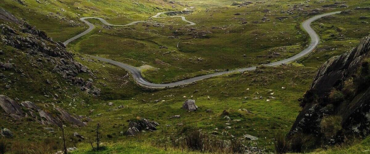 A winding mountain road through a valley with rocky terrain and grassy slopes.