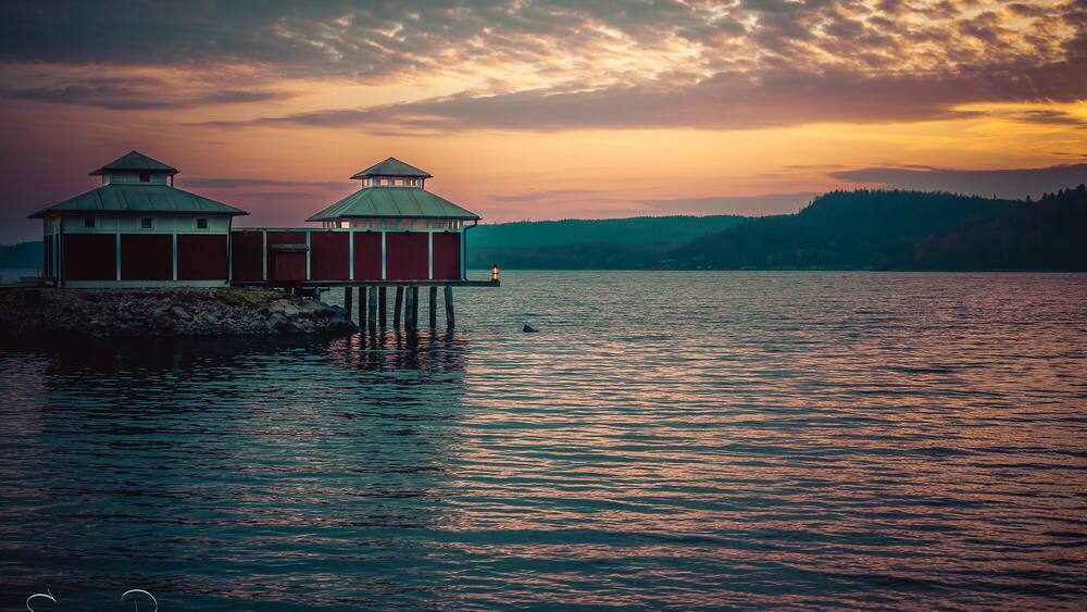 Une jetée avec deux bâtiments rouges et un phare, au coucher du soleil.