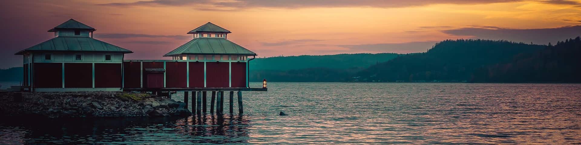 A pier with two red buildings and a lighthouse at sunset.