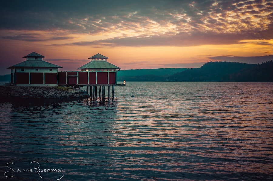 A pier with two red buildings and a lighthouse at sunset.