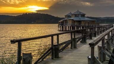 A wooden pier leading to a house by a lake at sunset.