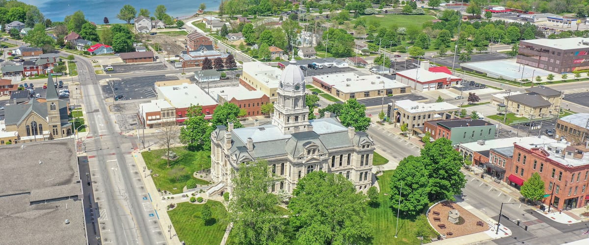 A town with a prominent historic building, a large body of water, and surrounding greenery.
