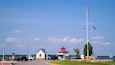 A lighthouse, a small building, a flagpole with flags, a one-way sign, and a body of water.