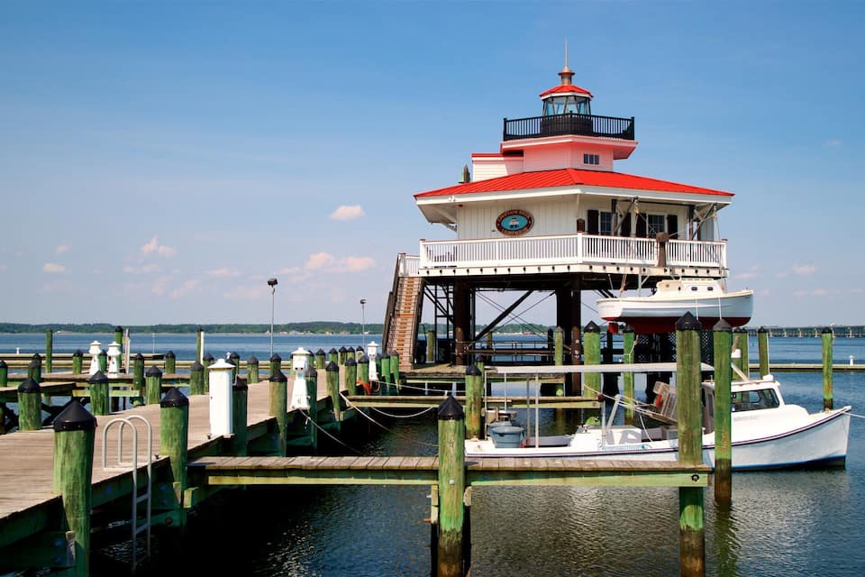 A lighthouse on a wooden pier with a boat docked nearby.