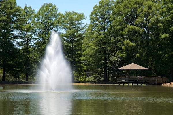 A fountain in a park with a gazebo in the background.