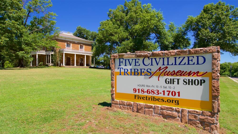 A sign for the Five Civilized Tribes Museum Gift Shop with a brick wall and a building in the background.