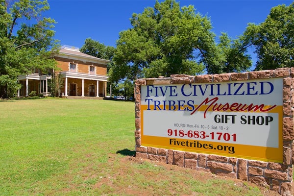 A sign for the Five Civilized Tribes Museum Gift Shop with a brick wall and a building in the background.