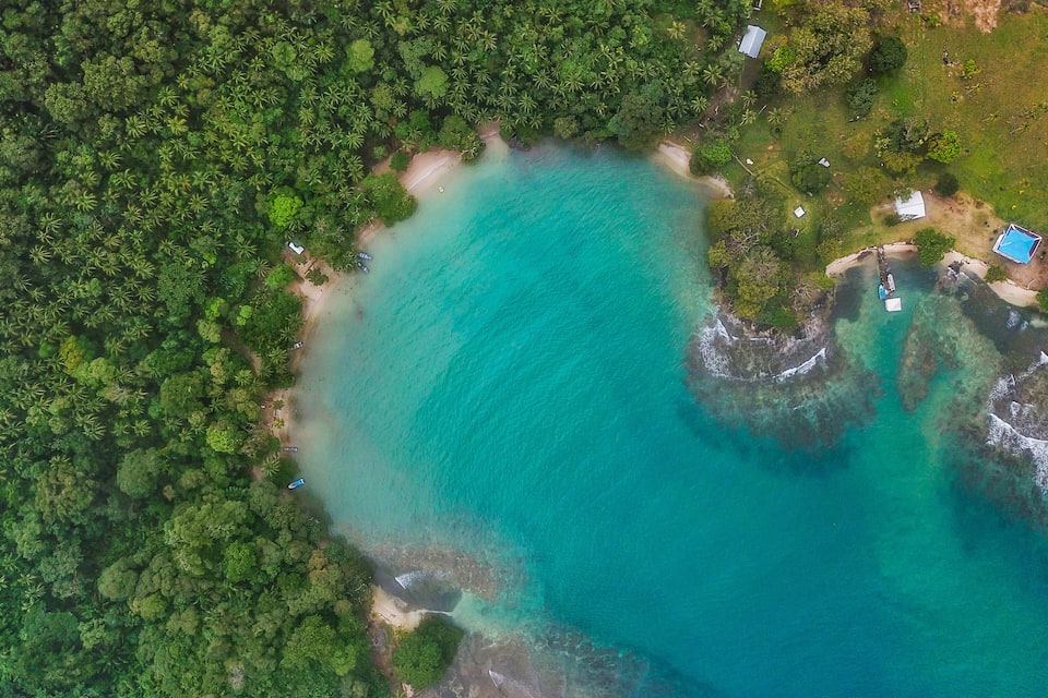 An aerial view of a turquoise beach surrounded by dense green forest.