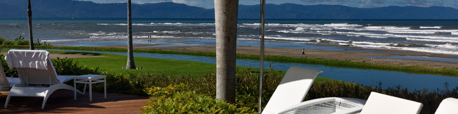 Um espaço de descanso à beira-mar com cadeiras e guarda-sóis brancos, com vista para o oceano e as montanhas.
