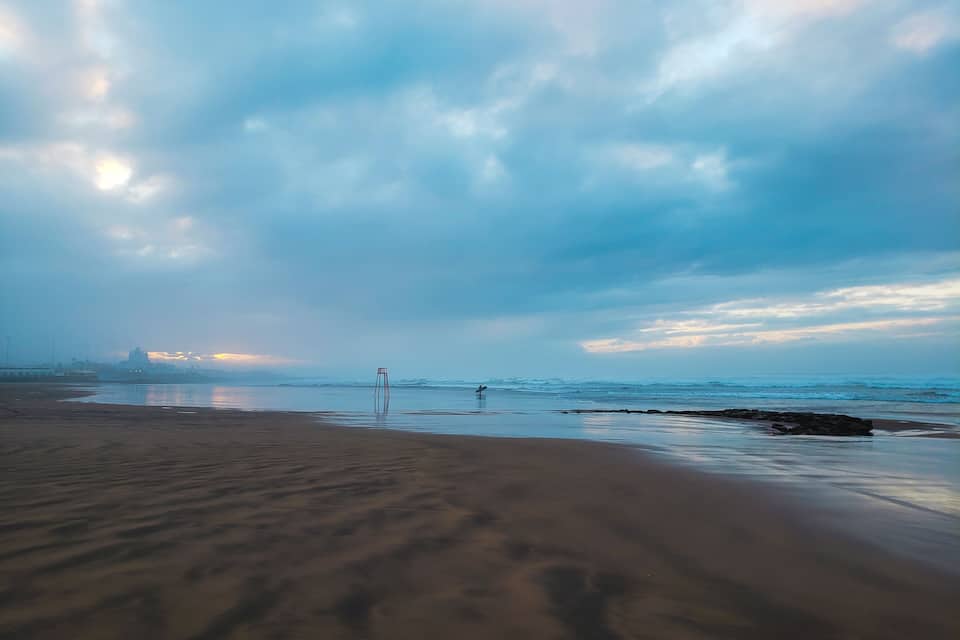 Una playa con una estructura metálica en el agua, olas y un cielo nublado.