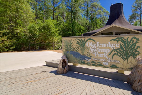 Et træskilt for Okefenokee Swamp Park, der viser et sumpområde og en bygning i baggrunden.