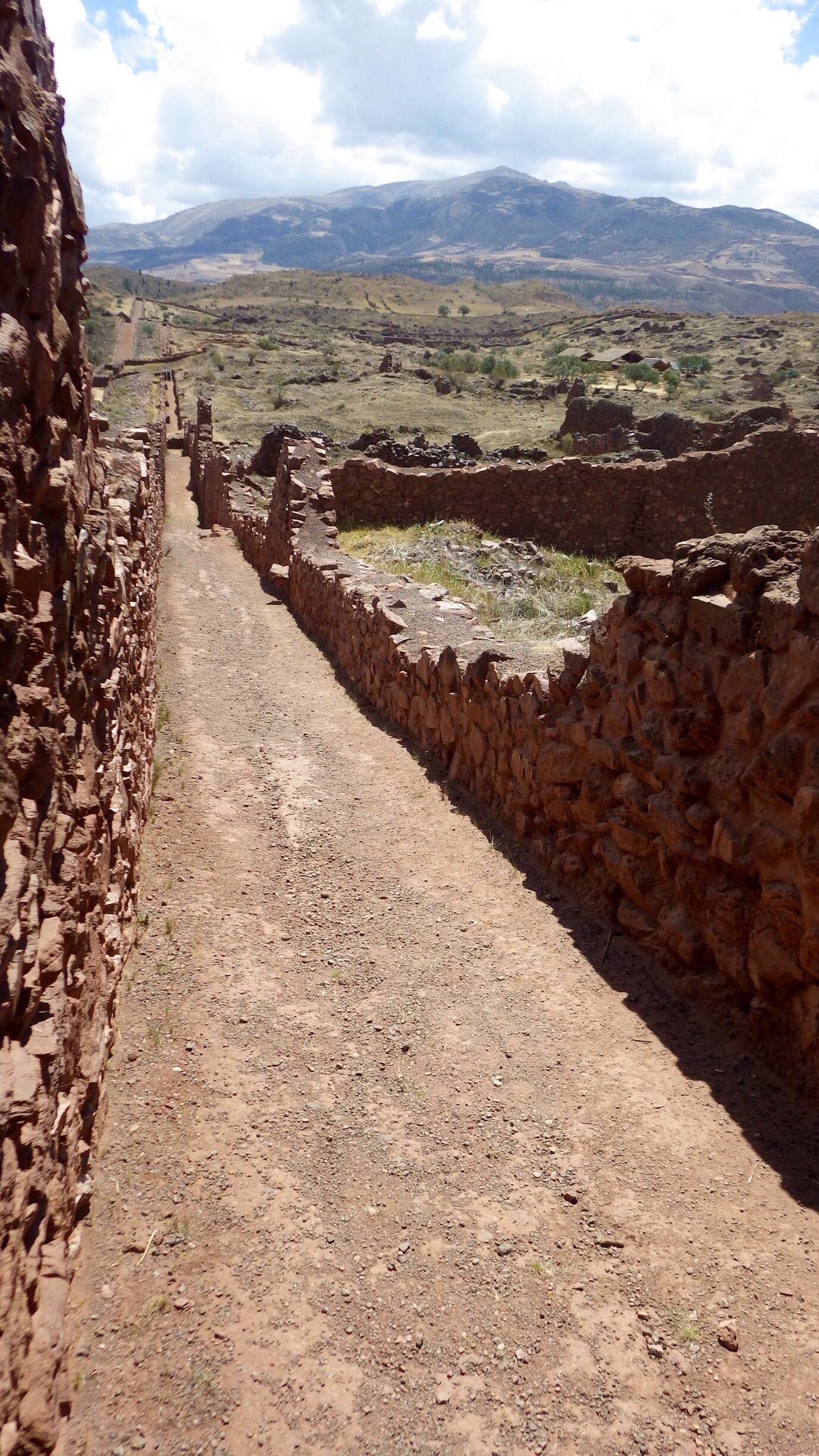 A stone pathway leading through an ancient ruin with a mountainous landscape in the background.