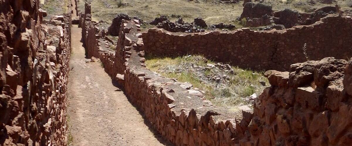 A stone pathway leading through an ancient ruin with a mountainous landscape in the background.