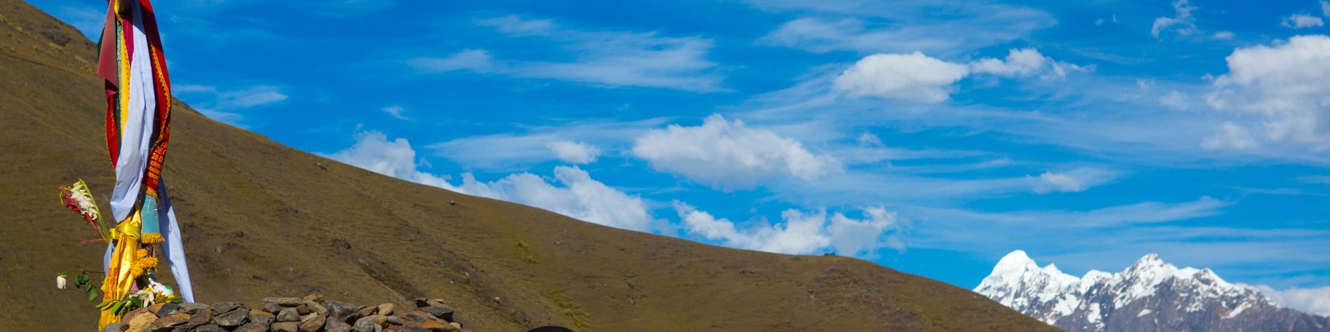 Un paisaje montañoso con cielo azul despejado, una construcción de piedra y una persona con un chal colorido.