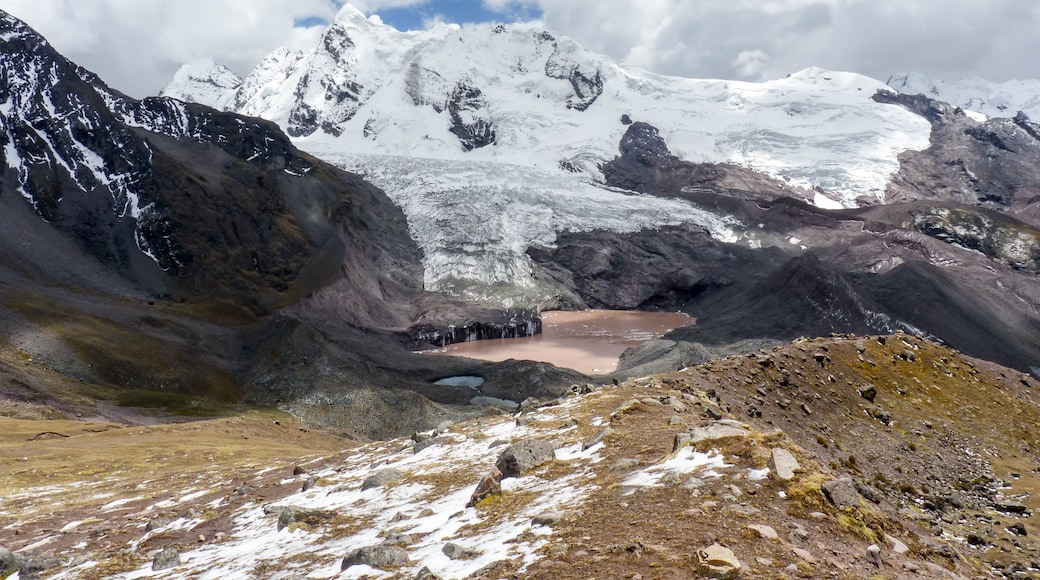 A glacier with a small lake, rugged mountains, and a cloudy sky.