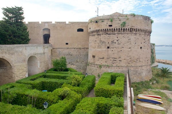 Um castelo histórico com fossado, jardins exuberantes e vista clara para o mar.
