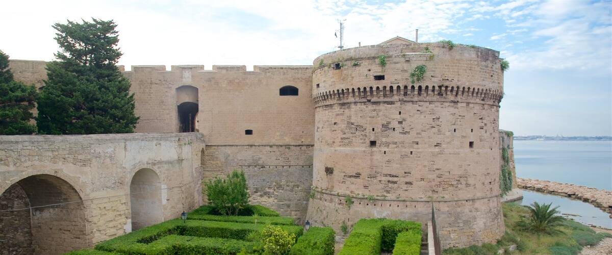 A historic castle with a moat, lush gardens, and a clear view of the sea.
