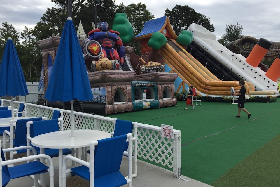 Ein Vergnügungspark im Freien mit Hüpfburgen, einem Piratenspielbereich und blau-weißen Sitzgelegenheiten.