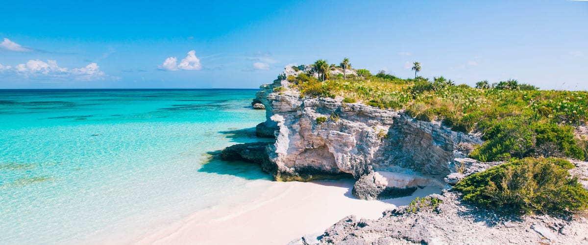 A clear turquoise sea, white sandy beach, and rocky cliffs with sparse vegetation.