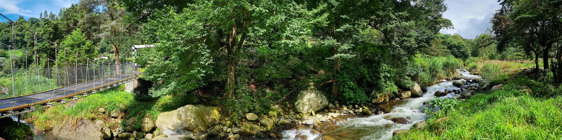 Um rio serpenteando por uma floresta, com uma ponte suspensa.