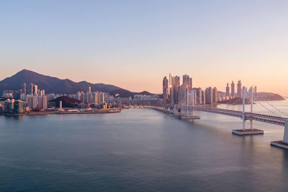 A cityscape with a prominent bridge spanning a body of water, surrounded by high-rise buildings and a mountain in the background.