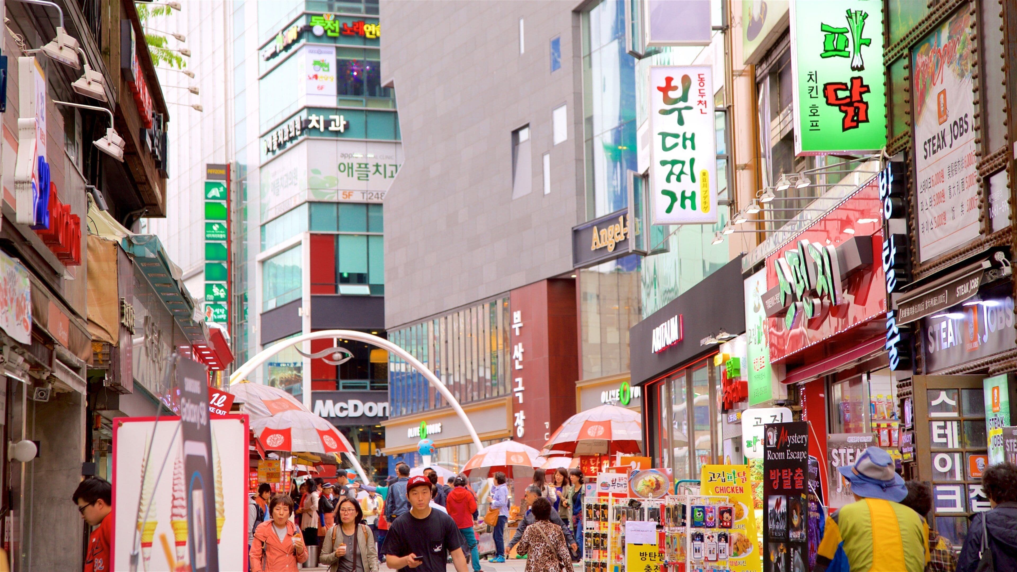 A busy urban street with various shops and signs, including a McDonald's and a store with a large 'Mystery Room Escape' sign.