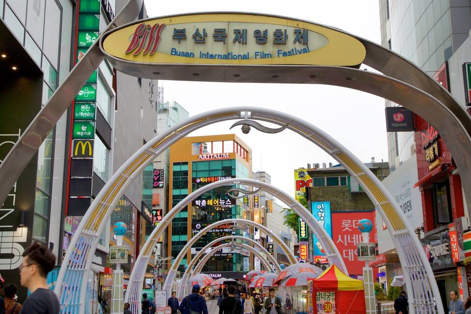 Una bulliciosa calle urbana con un gran arco que anuncia el Festival Internacional de Cine de Busan.